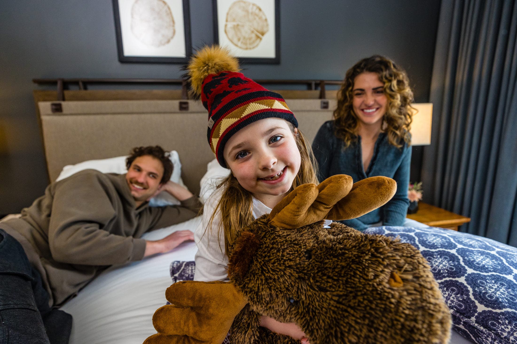 A close up of a family sitting on a queen bed in a suite having a fun time at Teton Mountain Lodge