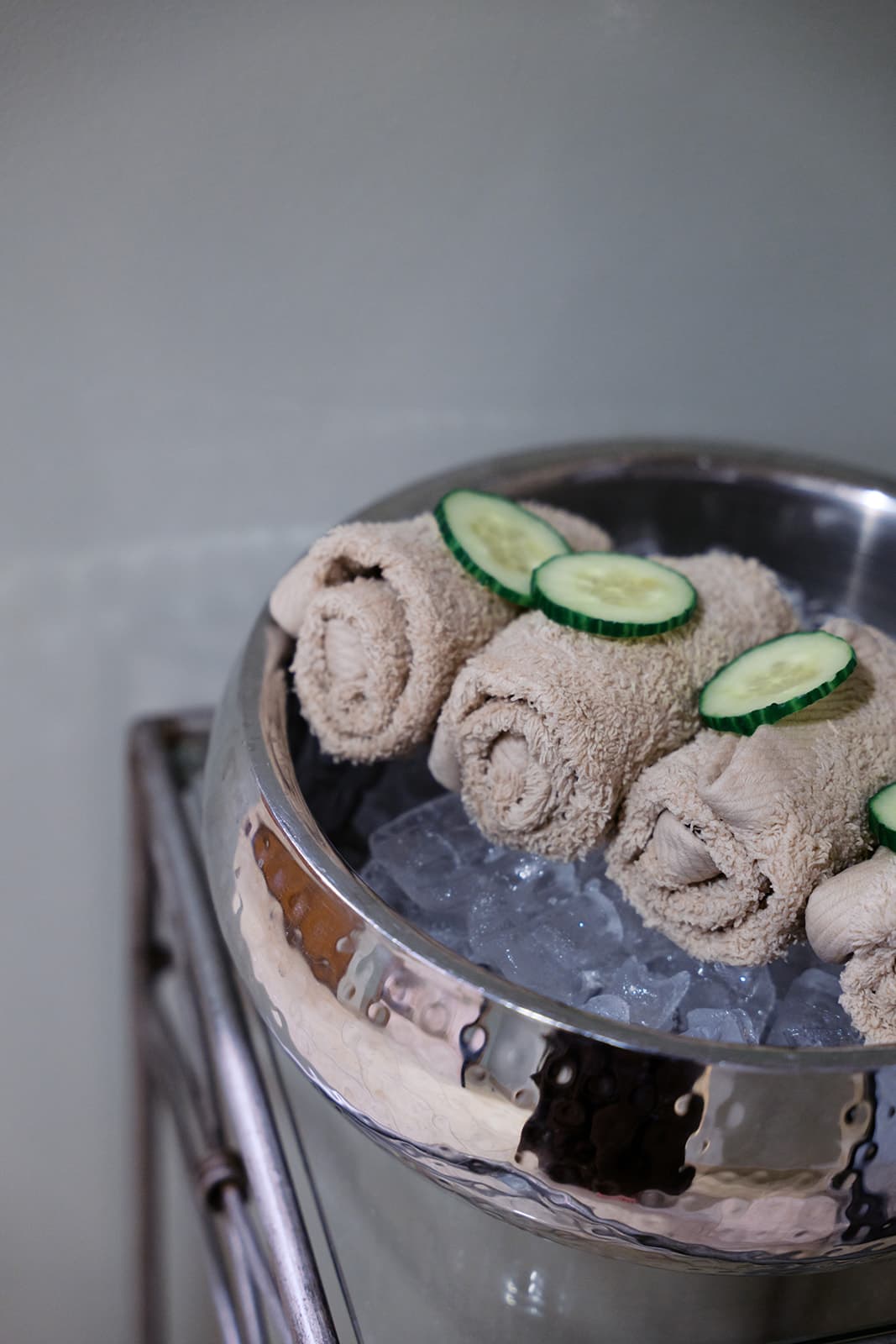 A photo of rolled-up towels sitting on a bed of ice, with slices of cucumber on top