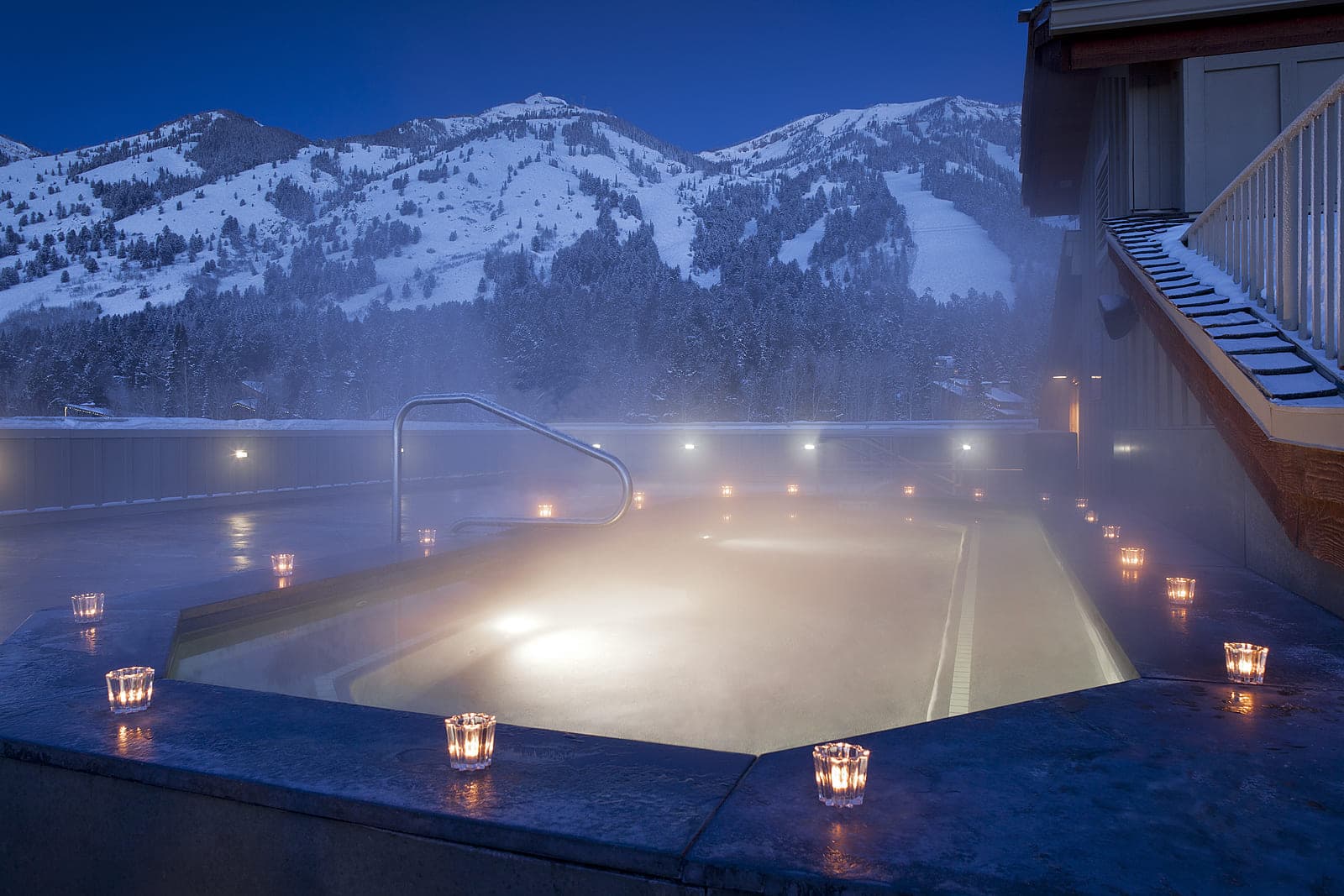 A misty Teton Mountain Lodge & Spa Rooftop Hot Tub with snow capped mountains in the background and tea lights surrounding the hot tub