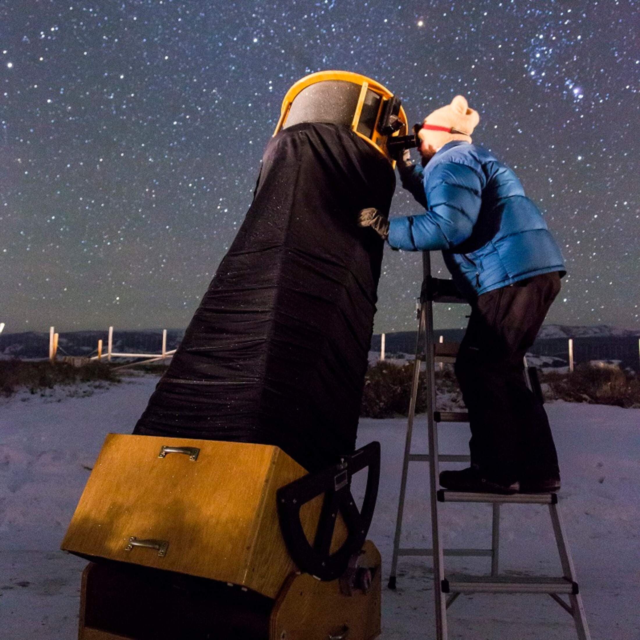 A person looks through a telescope at the stars in the Winter night sky.