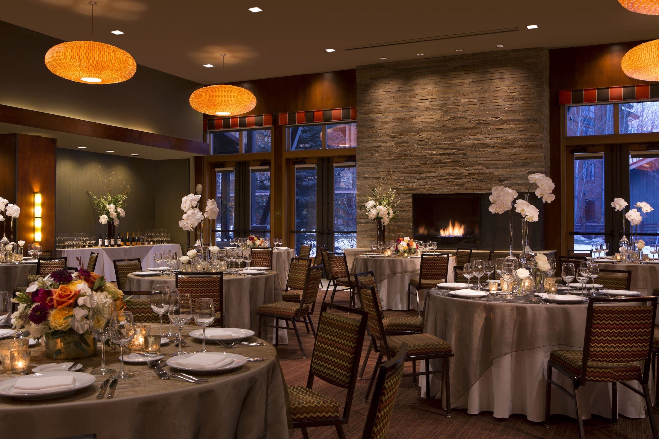 Murie Ballroom, multiple tables with place settings, at back between two windows is a fireplace, on the opposite wall is a self-serve bar