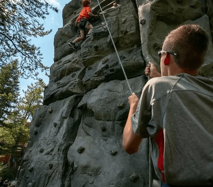 A person climbing an outdoor climbing wall while another person belays them