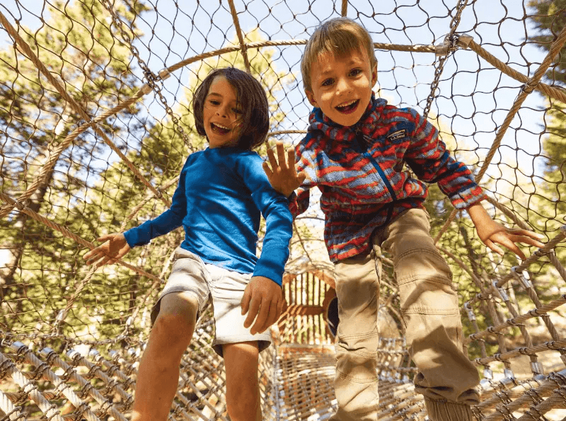 Two children play on an enclosed rope bridge at the Grand Adventure Camp
