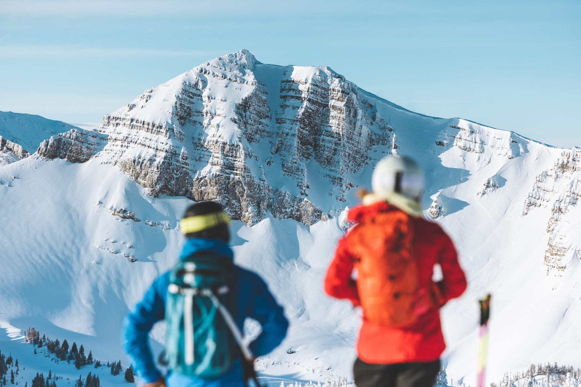 Two people in skiing gear observe a snow-covered mountain