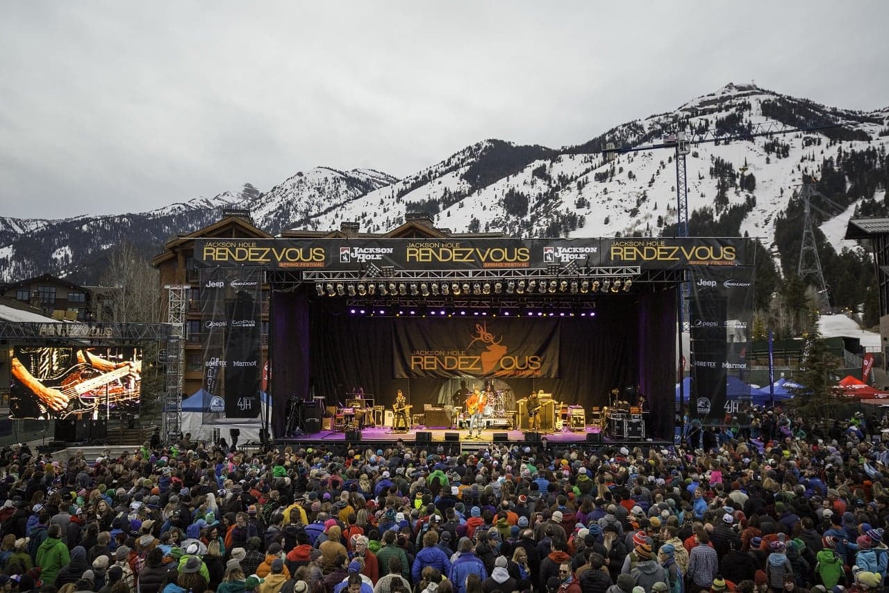 Crowd at the Jackson Hole Rendezvous Spring Festival concert in Teton Village, steps from Teton Mountain Lodge, with snow-capped peaks of Jackson Hole, Wyoming behind the stage
