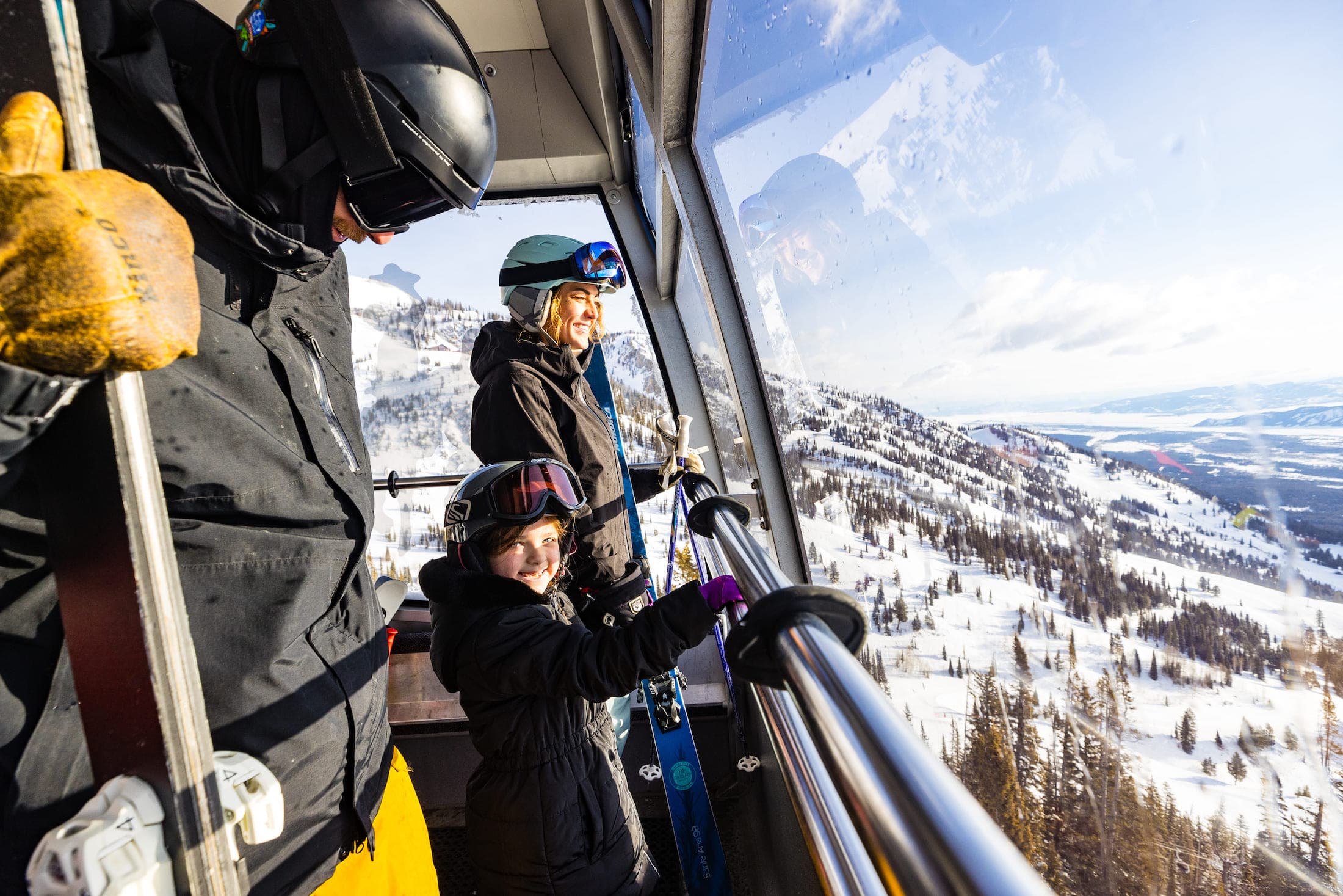 A mother, father and child looking out an aerial tram's window at the mountains near Teton Mountain Lodge