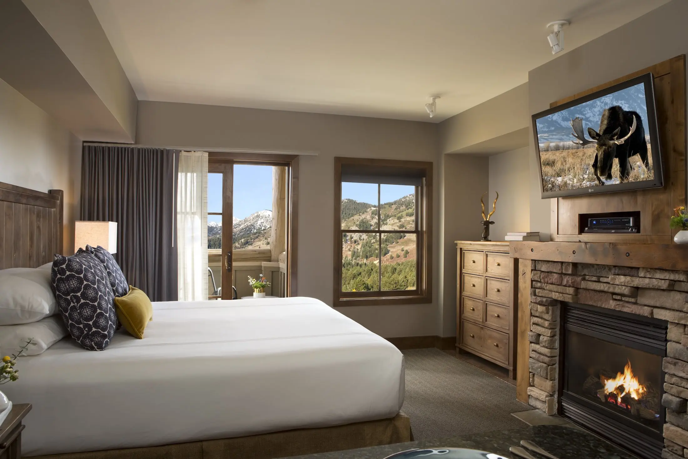 Teton Mountain Lodge Sundance Junior Suite with a large Tv above a fireplace, a balcony and a great view of the mountains