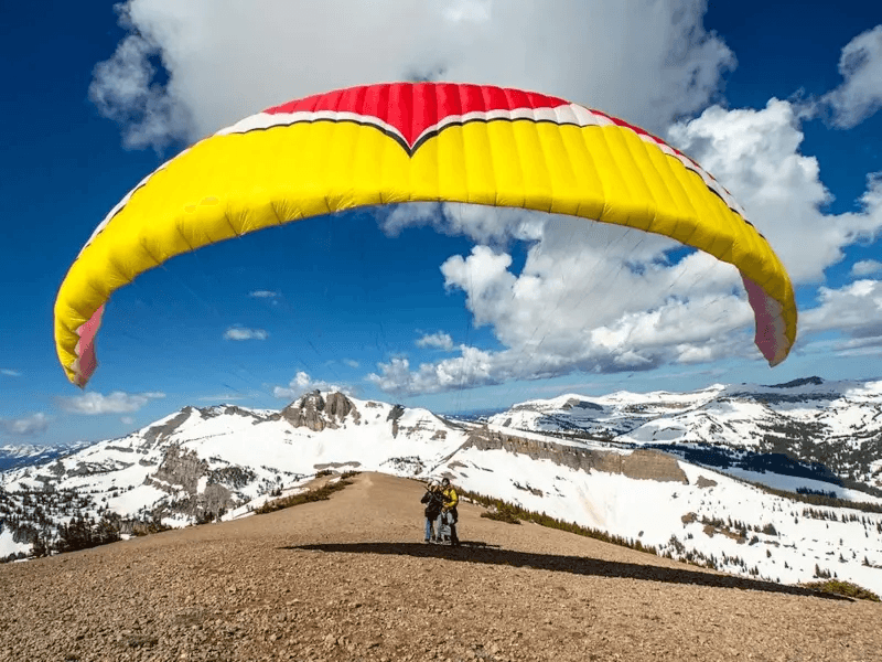 Two people standing on top of a mountain with a paragliding parachute open
