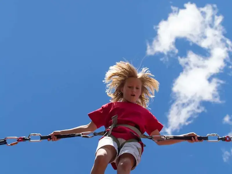 A young woman is bouncing on a bungee trampoline set against a blue sky