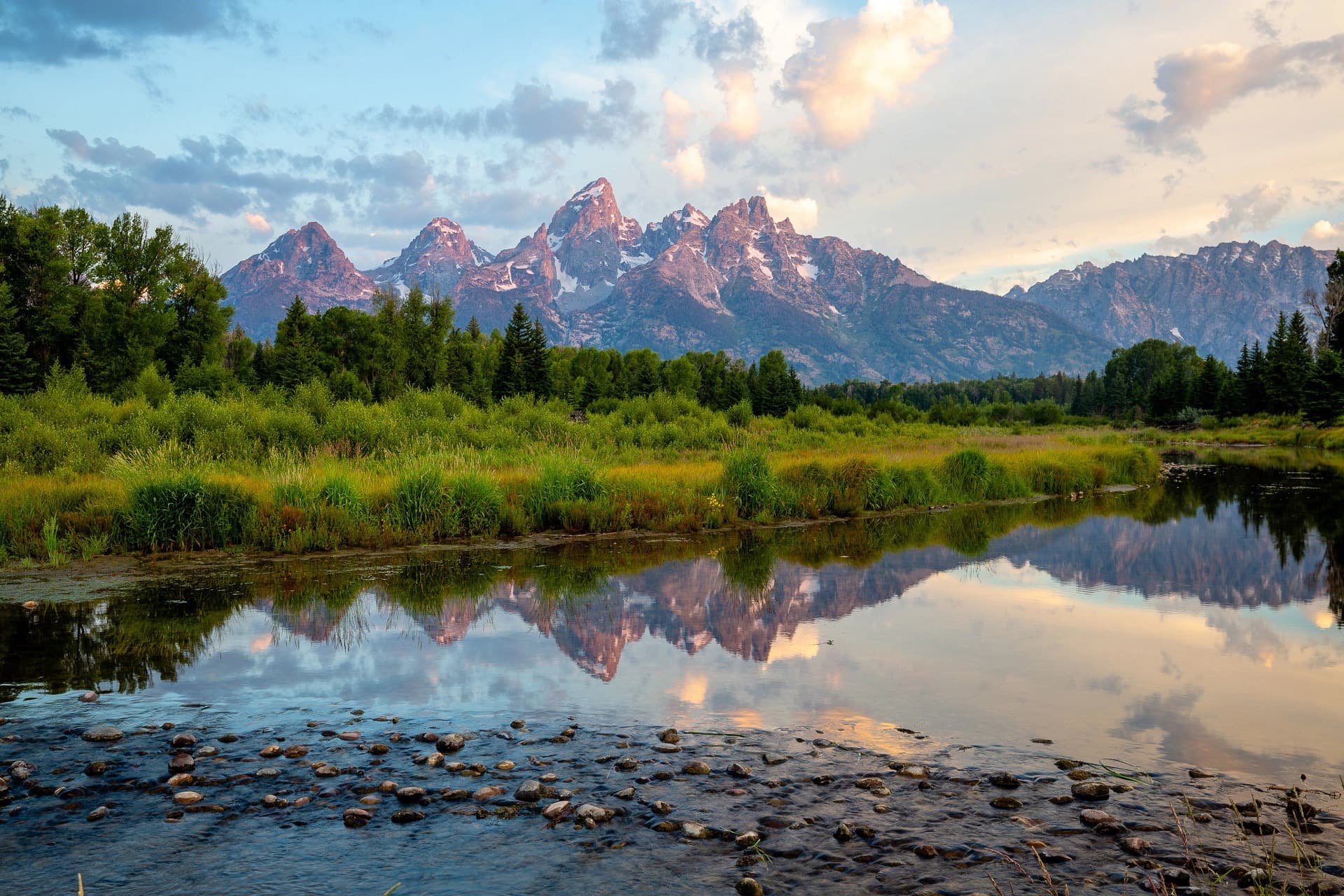Sunrise alpenglow on the Grand Teton range reflected in the Snake River near Teton Mountain Lodge in Jackson Hole, Wyoming
