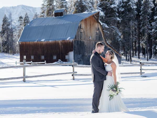 Bride and groom in the snow in front of a barn.