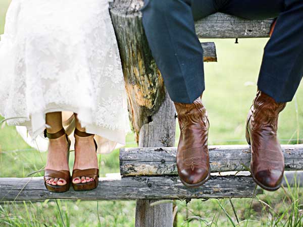 Bride And Groom With Boots Sitting On A Fence.
