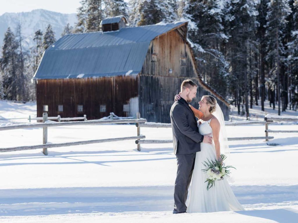 Bride and groom in the snow near an old barn.