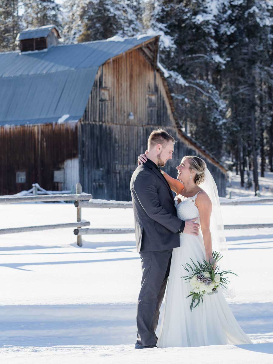 Bride and groom in the snow near an old barn.